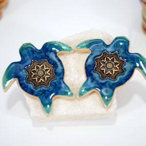 May include: Two blue and green ceramic turtle figurines with gold accents and a mandala design on their shells.