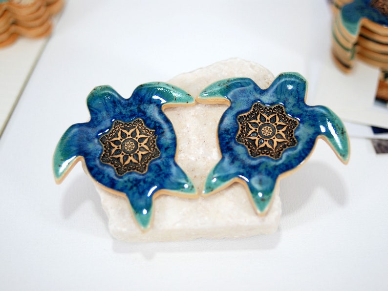May include: Two blue and green ceramic turtle figurines with gold accents and a mandala design on their shells.