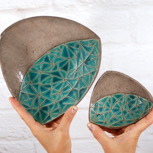 May include: Two triangular ceramic dishes with a teal geometric pattern. The larger dish is in the foreground and the smaller dish is behind it.