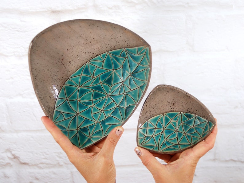 May include: Two triangular ceramic dishes with a teal geometric pattern. The larger dish is in the foreground and the smaller dish is behind it.