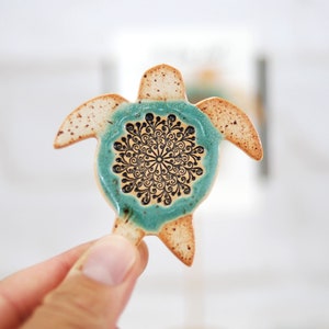 May include: A ceramic turtle figurine with a teal glaze and a black and white mandala design on its shell.