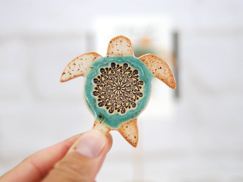 May include: A ceramic turtle figurine with a teal glaze and a black and white mandala design on its shell.