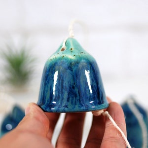 May include: A blue and green ceramic wind chime with a bell-shaped design. The chime is hanging from a white string.