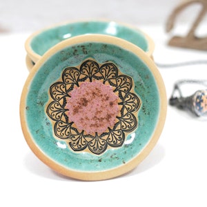 Peut inclure: Un petit plat en c&eacute;ramique avec un gla&ccedil;age vert turquoise et un motif de mandala noir et blanc. Le centre du mandala est un cercle rose.