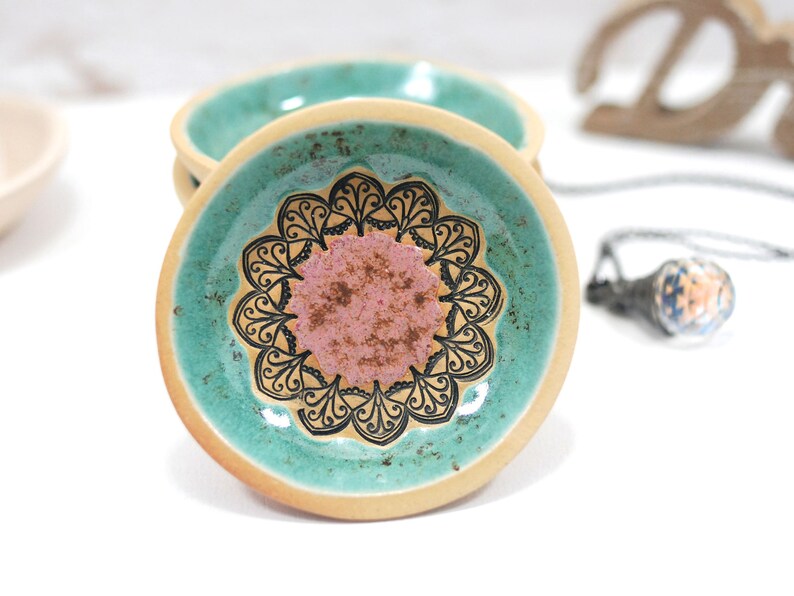 Peut inclure: Un petit plat en c&eacute;ramique avec un gla&ccedil;age vert turquoise et un motif de mandala noir et blanc. Le centre du mandala est un cercle rose.