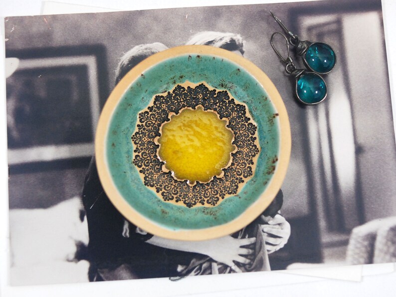 Peut inclure: Un petit plat en c&eacute;ramique avec un gla&ccedil;age bleu sarcelle et un motif de mandala noir et blanc. Le centre du mandala est un cercle jaune.