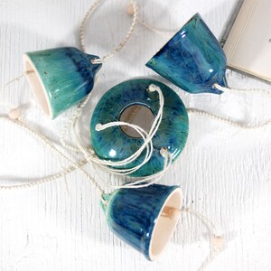 May include: A ceramic wind chime with four blue and green bells and a round, blue and green ceramic piece in the center. The bells are connected by white string.