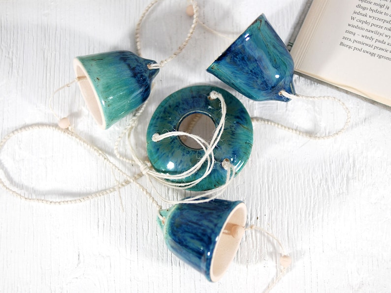 May include: A ceramic wind chime with four blue and green bells and a round, blue and green ceramic piece in the center. The bells are connected by white string.