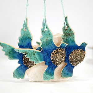 May include: Three ceramic dove ornaments with blue and green glaze and gold accents. Each dove has a mandala design on its chest.