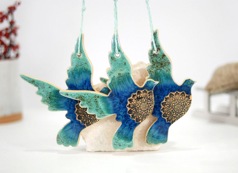 May include: Three ceramic dove ornaments with blue and green glaze and gold accents. Each dove has a mandala design on its chest.