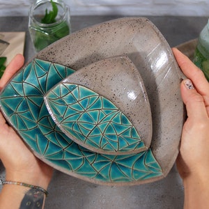 May include: Three ceramic bowls nested together. The largest bowl is gray with a speckled finish. The two smaller bowls are teal blue with a geometric pattern.