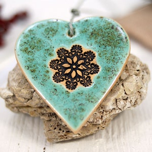 May include: A teal ceramic heart ornament with a black snowflake design. The ornament has a rustic, distressed look.