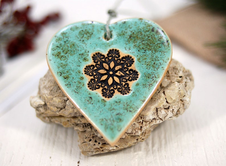 May include: A teal ceramic heart ornament with a black snowflake design. The ornament has a rustic, distressed look.