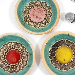 Peut inclure: Trois coupelles &agrave; bijoux en c&eacute;ramique turquoise avec des motifs de mandalas noirs et blancs. Chaque coupelle a un centre de couleur diff&eacute;rente&nbsp;: rose, rouge et jaune.