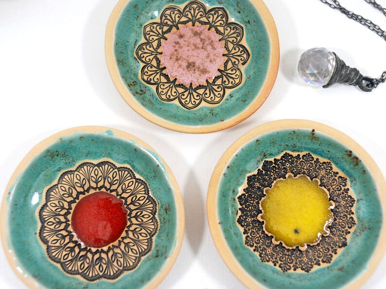Peut inclure: Trois coupelles &agrave; bijoux en c&eacute;ramique turquoise avec des motifs de mandalas noirs et blancs. Chaque coupelle a un centre de couleur diff&eacute;rente&nbsp;: rose, rouge et jaune.