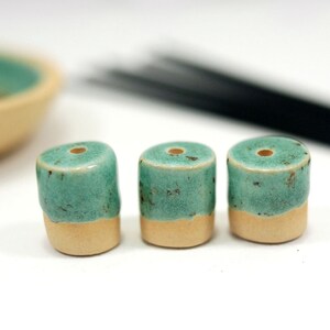 Peut inclure: Trois porte-encens en c&eacute;ramique bleu-vert et cr&egrave;me avec un trou sur le dessus. Les porte-encens sont dispos&eacute;s en rang&eacute;e sur une surface blanche.