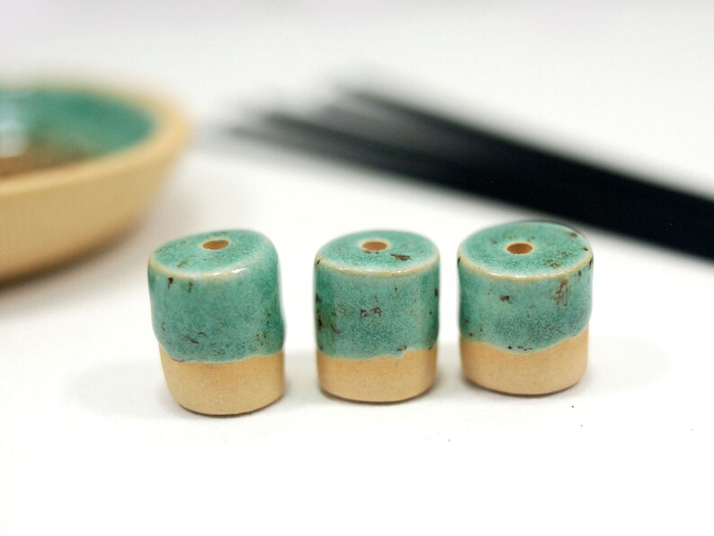Peut inclure: Trois porte-encens en c&eacute;ramique bleu-vert et cr&egrave;me avec un trou sur le dessus. Les porte-encens sont dispos&eacute;s en rang&eacute;e sur une surface blanche.