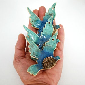 May include: Three ceramic blue and green birds with a mandala design on the bottom. The birds are stacked on top of each other and are being held in a hand.