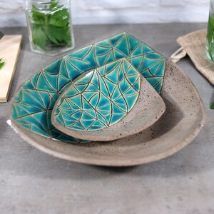 May include: Three ceramic serving dishes in a triangular shape. The dishes are gray with a teal geometric pattern. The dishes are nested together.