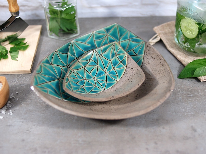 May include: Three ceramic serving dishes in a triangular shape. The dishes are gray with a teal geometric pattern. The dishes are nested together.