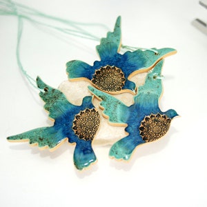 May include: Three ceramic dove ornaments with teal and blue glaze and gold accents. Each dove has a mandala design in the centre.