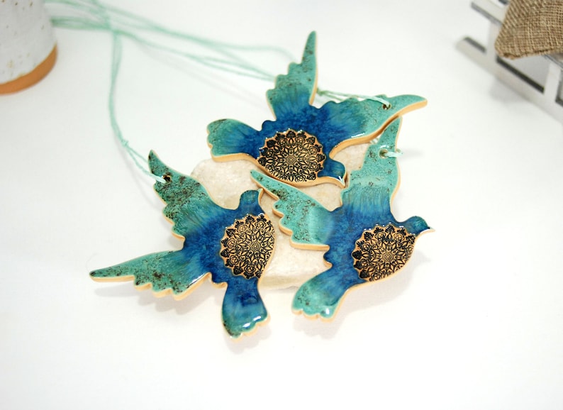 May include: Three ceramic dove ornaments with teal and blue glaze and gold accents. Each dove has a mandala design in the centre.