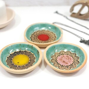 Peut inclure: Trois petits plats en c&eacute;ramique avec un gla&ccedil;age vert turquoise et des motifs de mandalas noirs. Chaque plat a un centre de couleur diff&eacute;rente&nbsp;: rouge, jaune et rose.