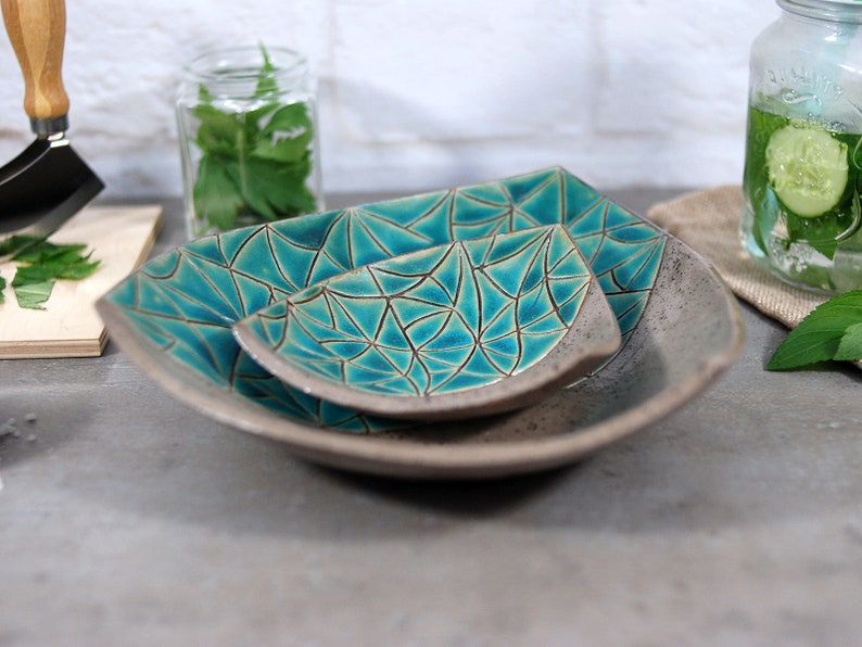 May include: Three ceramic bowls with a geometric pattern in shades of teal and gray. The bowls are nested together, with the smallest bowl on top.