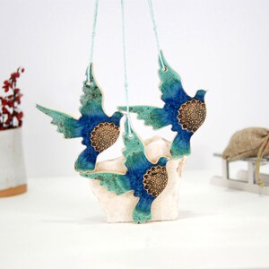 May include: Three blue and green ceramic doves with gold accents hanging from white strings. The doves are suspended from a white surface.