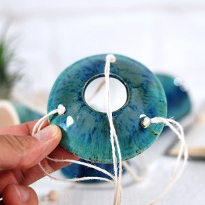 May include: A teal and blue ceramic planter with a hole in the center. The planter is suspended by white twine.
