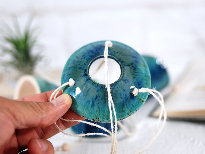 May include: A teal and blue ceramic planter with a hole in the center. The planter is suspended by white twine.