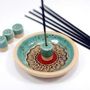 Peut inclure: Un porte-encens en c&eacute;ramique avec un motif turquoise et blanc. Le porte-encens a un motif de mandala rouge et noir au centre. Il y a quatre porte-b&acirc;tons d'encens turquoise et blanc sur le c&ocirc;t&eacute; de l'assiette.