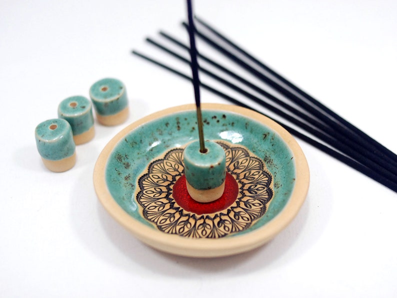 Peut inclure: Un porte-encens en c&eacute;ramique avec un motif turquoise et blanc. Le porte-encens a un motif de mandala rouge et noir au centre. Il y a quatre porte-b&acirc;tons d'encens turquoise et blanc sur le c&ocirc;t&eacute; de l'assiette.