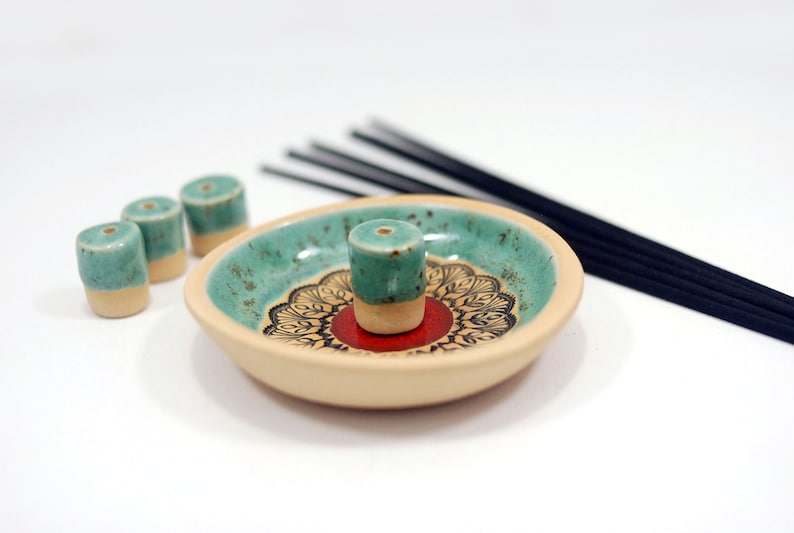 Peut inclure: Un porte-encens en c&eacute;ramique avec un gla&ccedil;age turquoise et cr&egrave;me. Le porte-encens a un motif de mandala rouge et noir et est livr&eacute; avec quatre c&ocirc;nes d'encens turquoise et cr&egrave;me.
