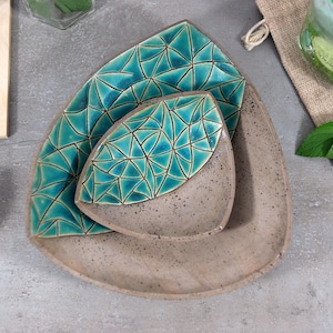 May include: Three triangular ceramic dishes nested together. The dishes are a light brown color with a speckled finish. The top two dishes have a teal blue geometric pattern.