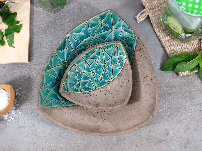 May include: Three triangular ceramic dishes nested together. The dishes are a light brown color with a speckled finish. The top two dishes have a teal blue geometric pattern.