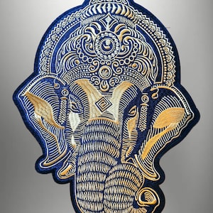 Op de afbeelding: Geborduurde patch met een olifantenontwerp in marineblauw en goud. De patch heeft gedetailleerde borduursels van een olifantenkop, oren en slurf, met een decoratieve rand. Het ontwerp is symmetrisch en sierlijk, geschikt voor kleding of accessoires.
