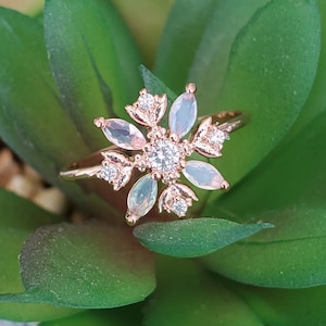 May include: A rose gold ring with a flower design featuring clear and white stones.