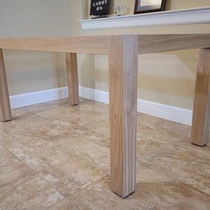 May include: A light wood dining table with four legs. The table is made of solid wood and has a natural finish. The table is sitting on a tiled floor.