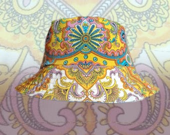 May include: A bucket hat featuring a vibrant, multi-colored paisley pattern in shades of yellow, orange, pink, and teal. The design consists of intricate floral and teardrop motifs arranged in a symmetrical, repeating layout across the crown and brim.