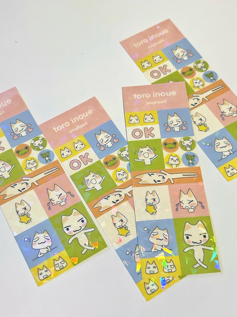 May include: A set of four holographic sticker sheets featuring a cartoon cat with different expressions. The stickers are on a light blue, yellow, and pink background. The text on the stickers reads "toro inoue" and "jxnghuart".