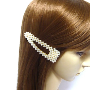 以下が含まれることがあります： 白い真珠で飾られた金色のヘアクリップ。クリップは、湾曲したエッジを持つ長方形の形をしています。
