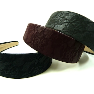 May include: Three wide headbands in black, burgundy, and dark grey, each featuring a lace pattern. The headbands have a padded design and a neutral-coloured interior lining. They are displayed against a white background.