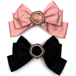 Könnte beinhalten: Zwei große Satinbänder mit juwelenbesetzten Mittelstücken. Das obere Band ist rosa und das untere Band ist schwarz.