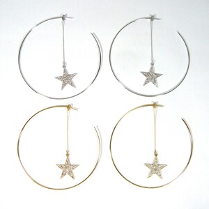 May include: A pair of hoop earrings with a dangling star charm. The earrings are available in gold and silver.