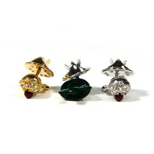 May include: Three decorative pin backs with a jeweled top and a metal base. The pin backs are gold, silver, and green.