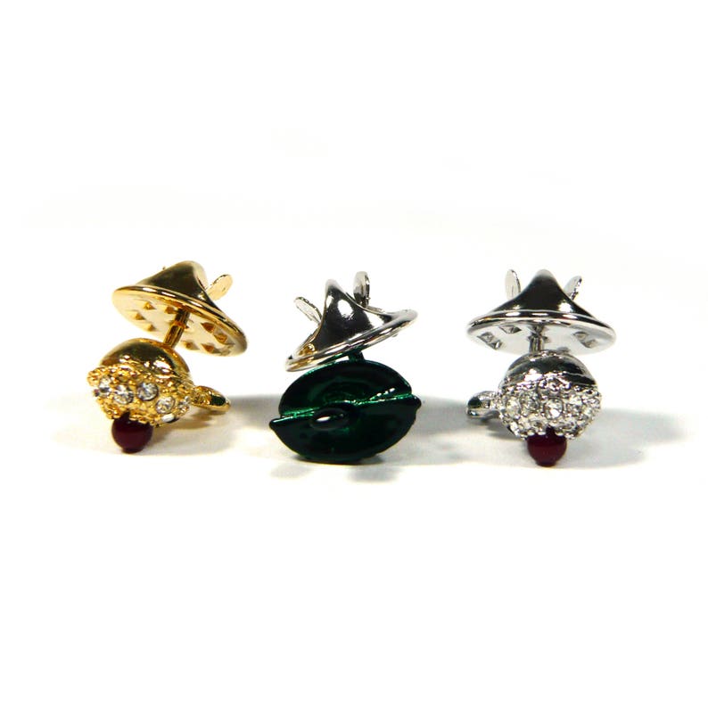 May include: Three decorative pin backs with a jeweled top and a metal base. The pin backs are gold, silver, and green.