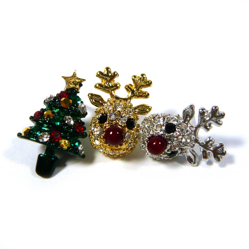 May include: Three Christmas-themed brooches: a green Christmas tree with red and white rhinestones, a gold reindeer with red rhinestones, and a silver reindeer with red rhinestones.