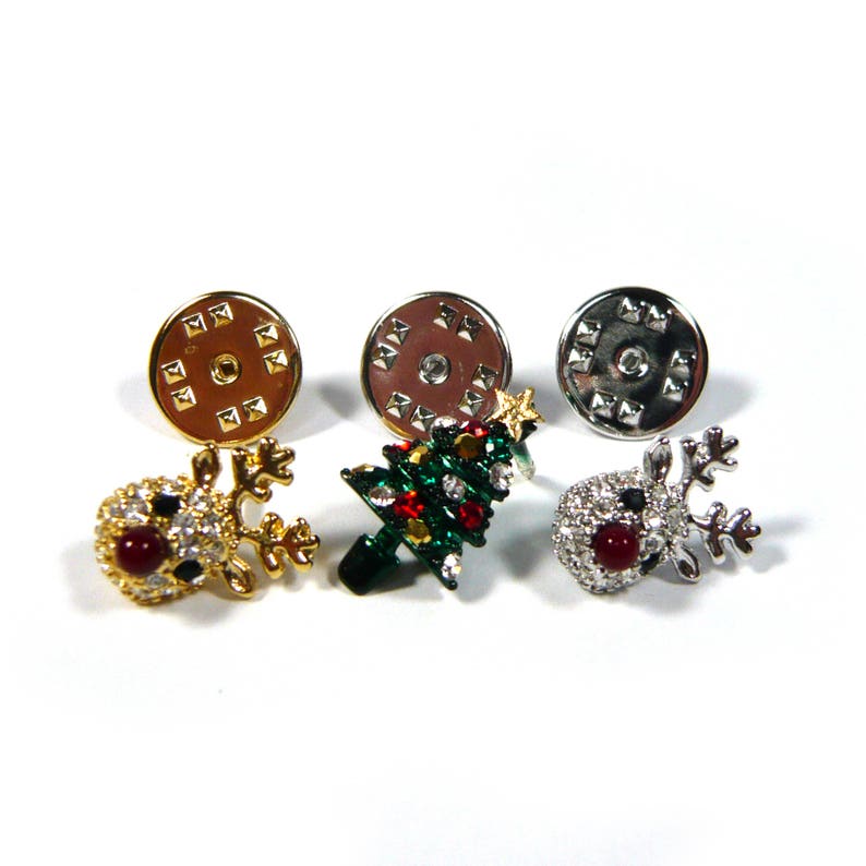 May include: Three Christmas themed pin back buttons. One features a gold reindeer with red rhinestones, another a green Christmas tree with red and white rhinestones, and the last a silver reindeer with red rhinestones.