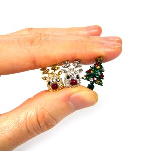 May include: Three Christmas-themed charms: two reindeer with red noses and rhinestones, one gold, one silver, and a green Christmas tree with red and gold ornaments.